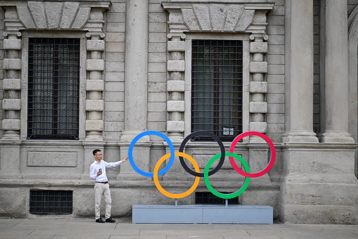 A man poses for a photograph in front of an installation depicting the Olympic Rings.