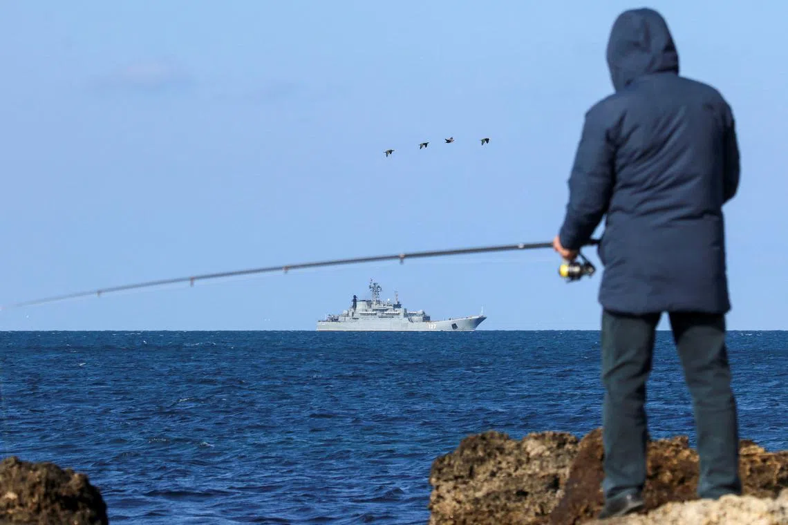 FILE PHOTO: A man fishes on the shore as an amphibious assault ship of the Russian Navy sails near the Black Sea port of Sevastopol, Crimea February 16, 2022. REUTERS/Alexey Pavlishak/File Photo