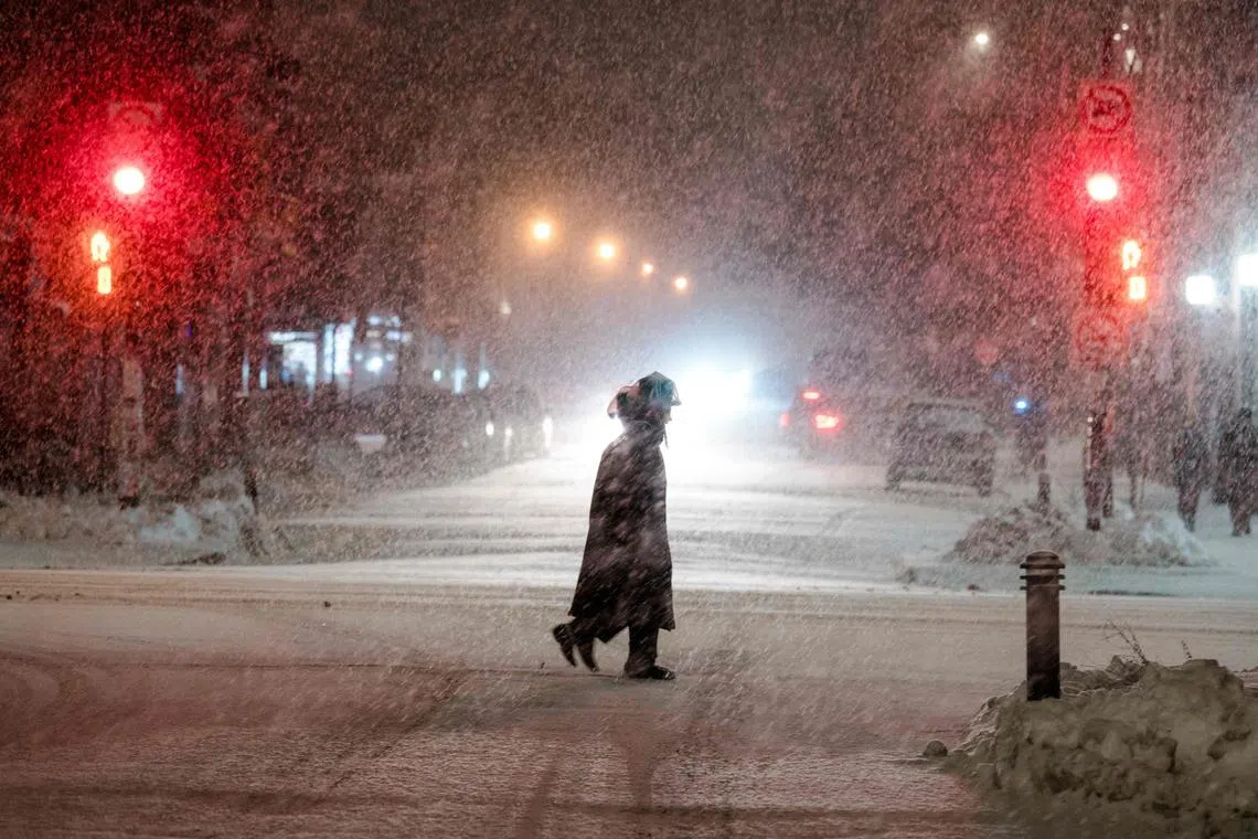 People cross a street in the Mile End, a borough in Montreal, Quebec, Canada, as the snow comes down on Dec 22, 2022.