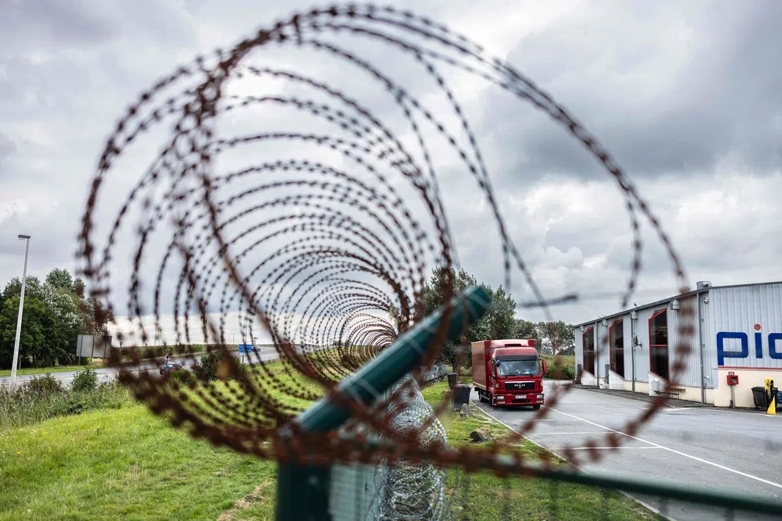 This photograph taken on August 28, 2023, shows a barbed wire fence displayed around a lorry parking in Marck, northern France, to prevent migrants from hiding in the lorries heading to Britain. All along the 130 km or so of coastline between Dunkirk and the Bay of the Somme, and even as far as Normandy, the authorities are combing the land and sky to try and stop people heading for the English coast. (Photo by Sameer Al-DOUMY / AFP)