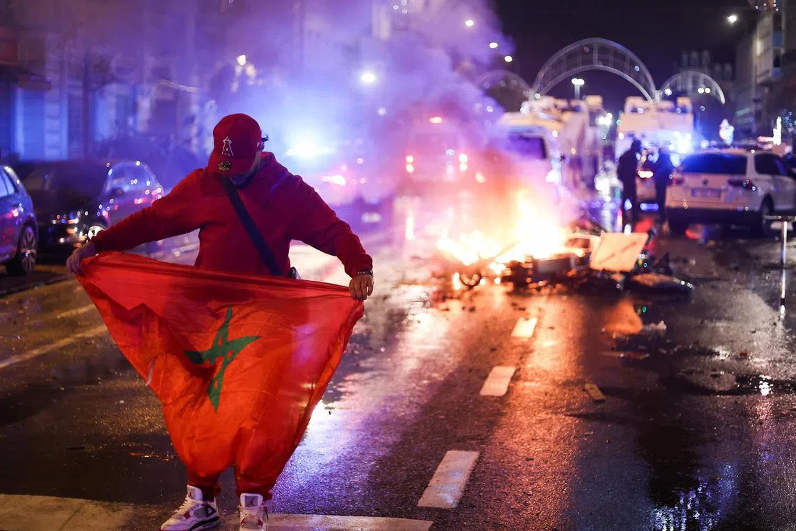 A fan holds a Moroccan flag as electric scooters burn in the back on the sidelines of the live broadcast of the World Cup Group F football match between Belgium and Morocco, in Brussels, on Nov 27.