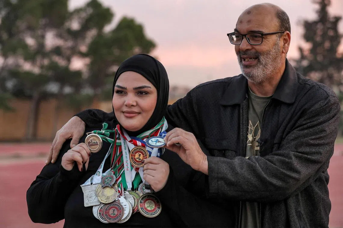 Rataj al-Sayeh poses with her medals next to her father during a training session near the edge of a dilapidated running track at the Tripoli Sports City in Tripoli.