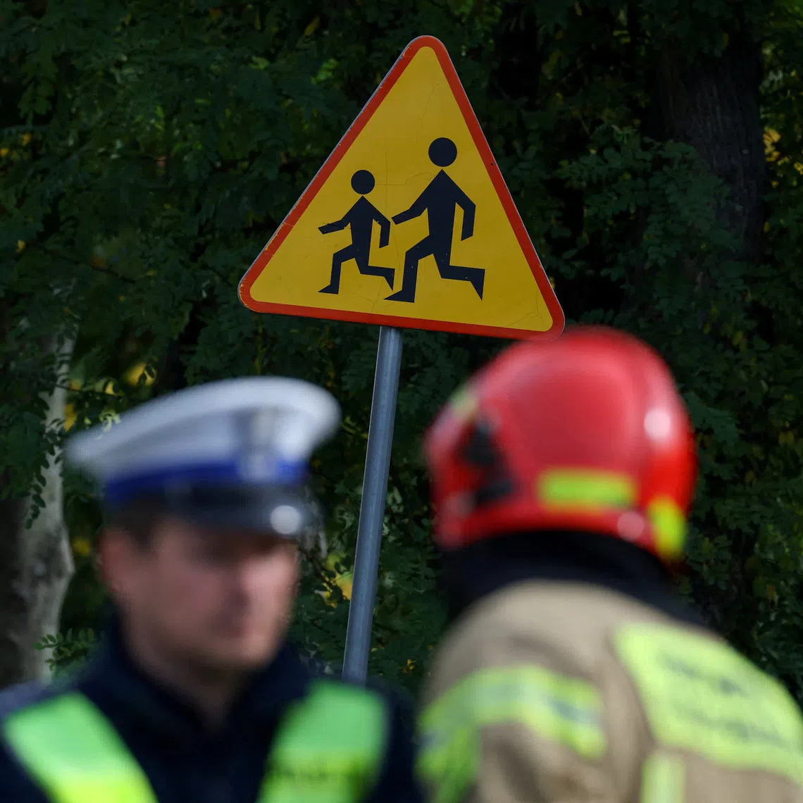 A police officer and a fire fighter stand near a road sign as they work at the site of a deadly attack at a school by a 15-year-old former pupil, in Leszczydol-Nowiny, Wyszkow County, northeast of Warsaw, Poland, October 8, 2026. REUTERS/Kacper Pempel