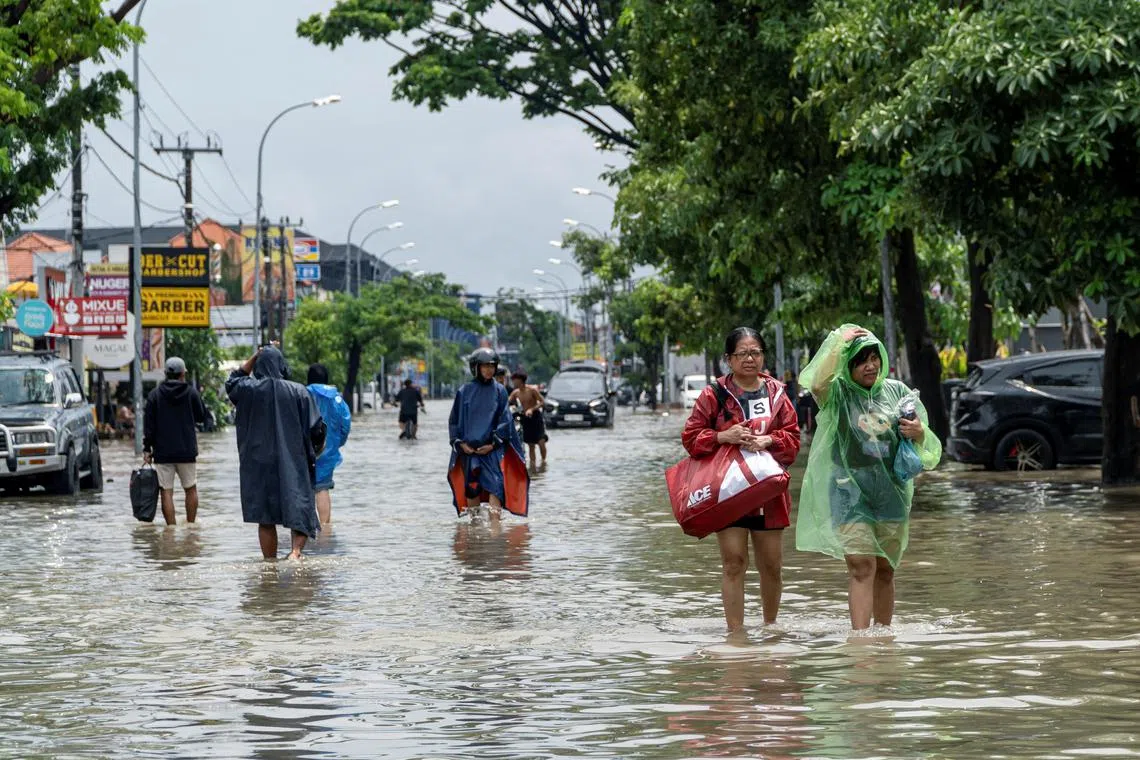 People carrying their belongings wade through a flooded street following overnight heavy rains in Legian, Badung, Bali, Indonesia September 10, 2025. REUTERS/Dicky Bisinglasi