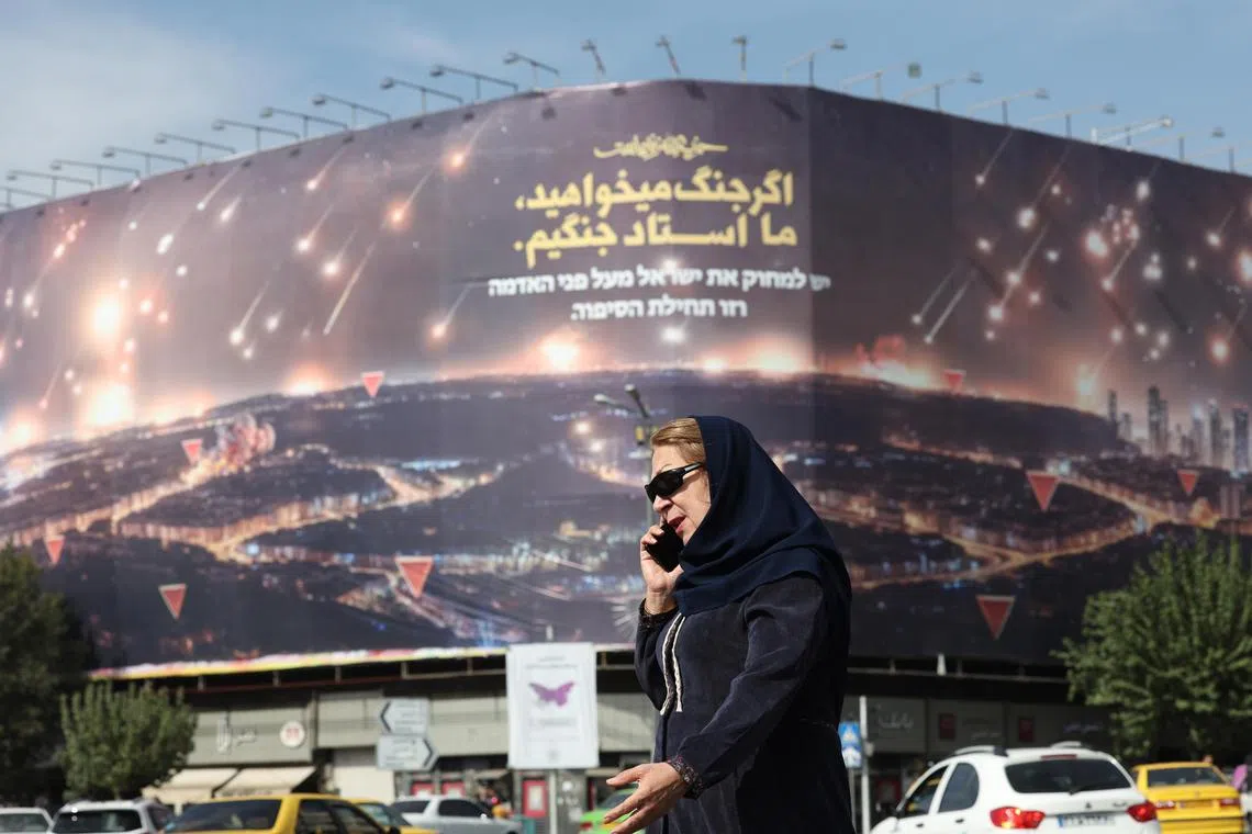 An Iranian woman walking near an anti-Israel billboard depicting Iran's recent missile attack on Israel and a sentence reading in Persian, "If you want war, we are the master of war", in Tehran, on Oct 26.