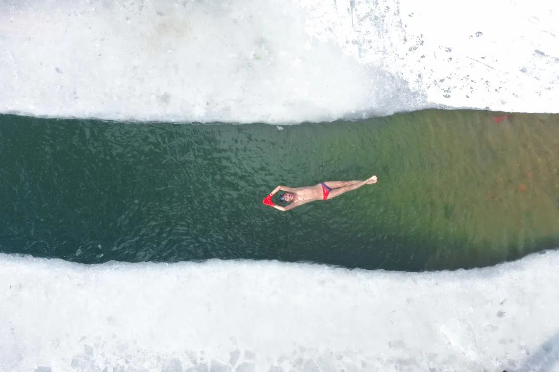 This aerial photo taken on December 21, 2022 shows a winter swimming enthusiast swimming in a partly frozen lake after snowfall in Shenyang, in northeastern China's Liaoning province. 
