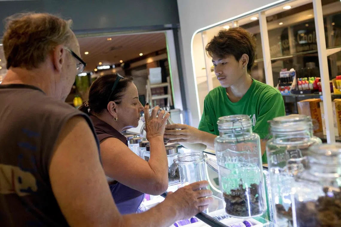 Customers smell a container of cannabis buds at a dispensary in Bangkok on November 22, 2022. (Photo by Jack TAYLOR / AFP)