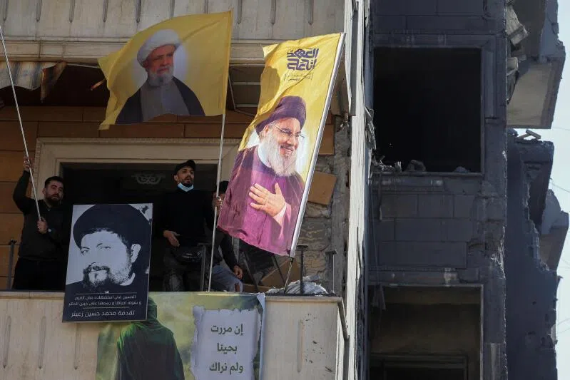 Hezbollah supporters looking out of a building damaged in an Israeli strike, with flags showing images of Hezbollah leaders Naim Qassem and Hassan Nasrallah at the site of an Israeli strike, in Choueifat, Lebanon, April 13, 2026.