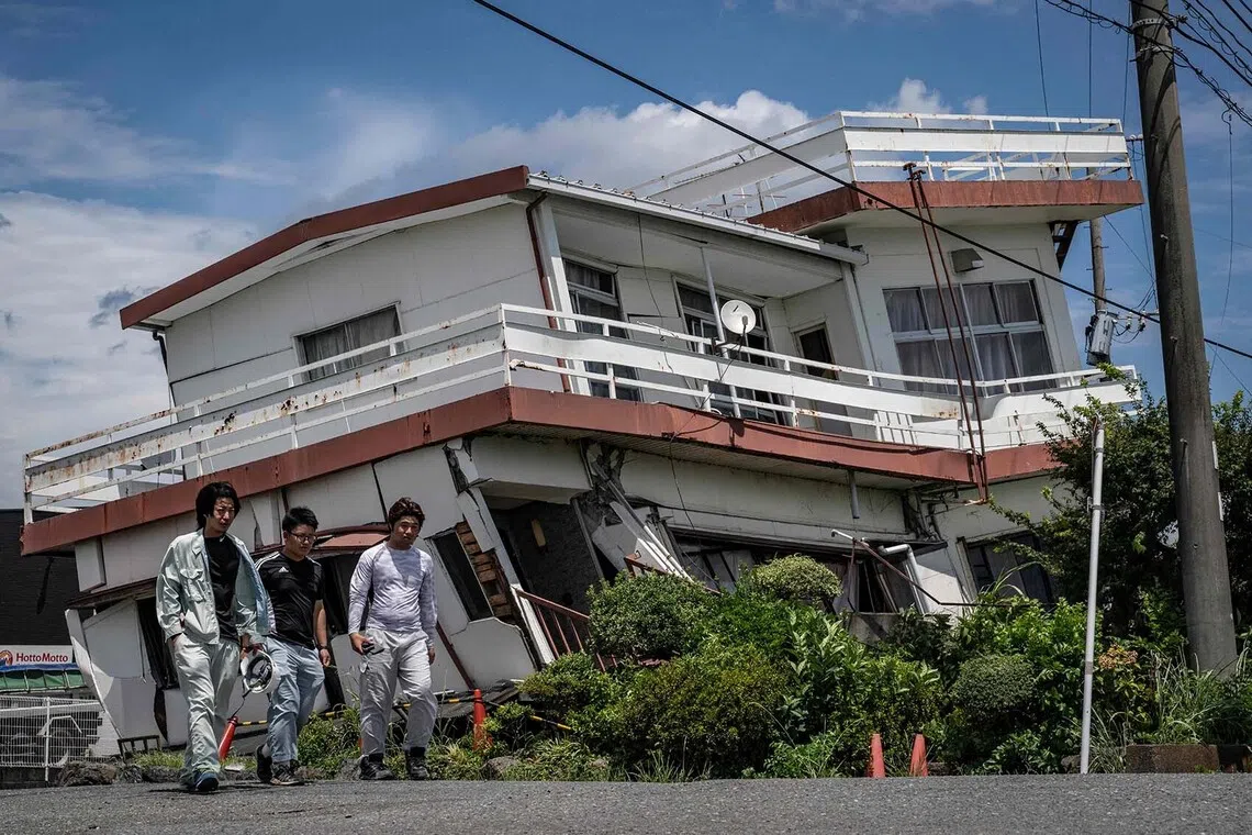 TOPSHOT - Workers walk past a damaged house and partially collapsed in Yatsushiro, Kumamoto prefecture on July 29, 2026, after an earthquake struck southwestern Japan the previous day. (Photo by Yuichi YAMAZAKI / AFP)
