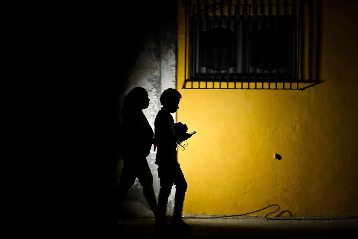 TOPSHOT - A woman holds a flashlight while walking with a man on a street during a blackout in Havana on March 16, 2026. Cuba suffered a widespread power cut on March 16, 2026, according to the national electricity company, against the backdrop of a severe crisis on the island caused by the US energy blockade. (Photo by Yamil LAGE / AFP)