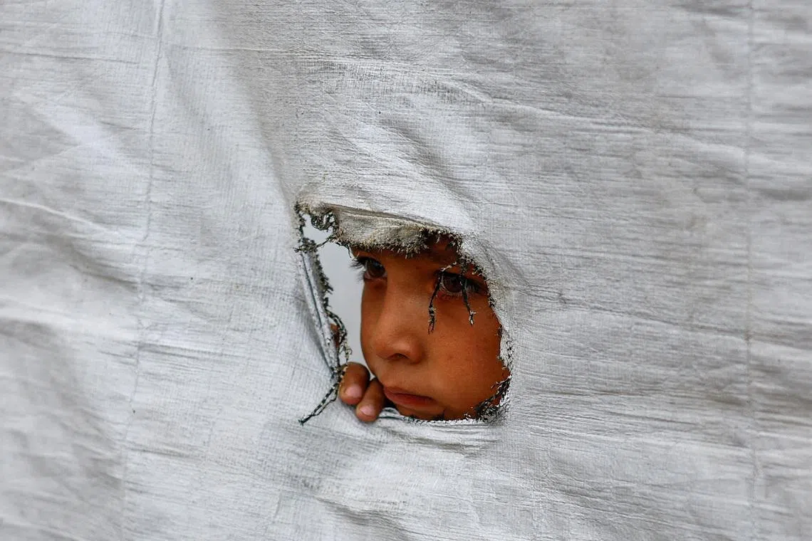 A displaced Palestinian boy peering through a tear in a tent wall, in Gaza City, on May 6, 2026. 