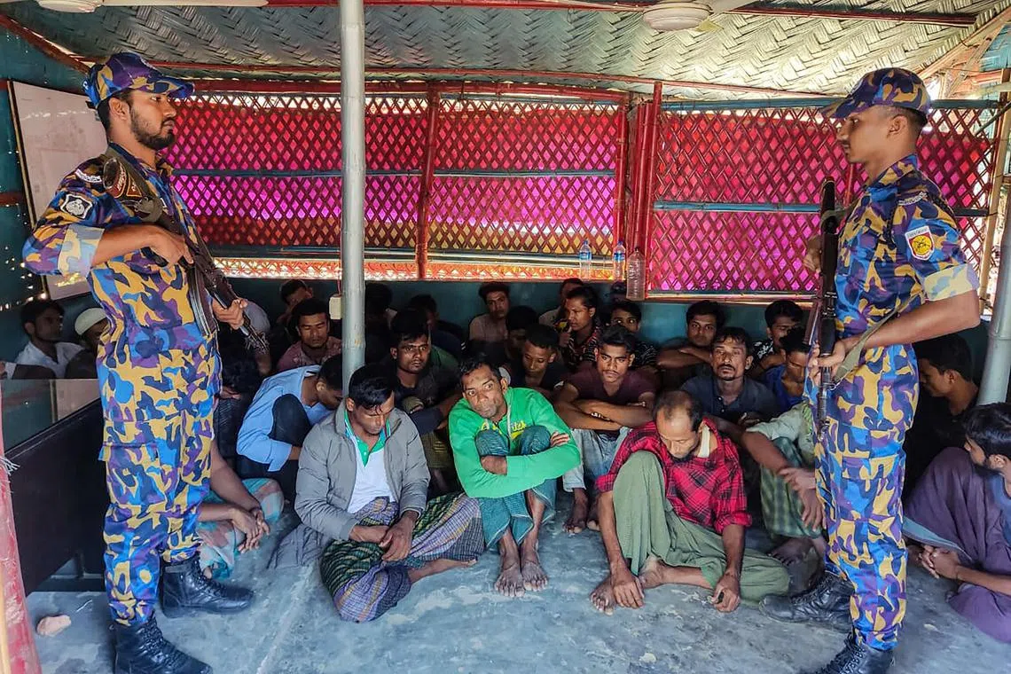 Rohingya refugees sit next to security personal after crackdown in Rohingya refugee camp in Ukhia, on Oct 28, 2022.