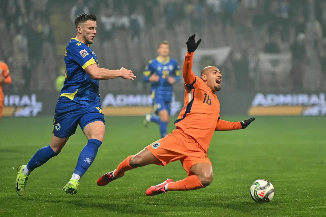 Netherlands forward Donyell Malen (right) falls to the ground under pressure from Bosnia and Herzegovina forward Ermedin Demirovic (left).