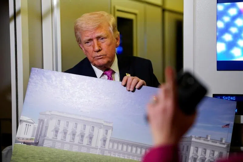 US President Donald Trump speaking to the media while holding up renderings of the planned White House ballroom, aboard Air Force One on March 29, 2026.