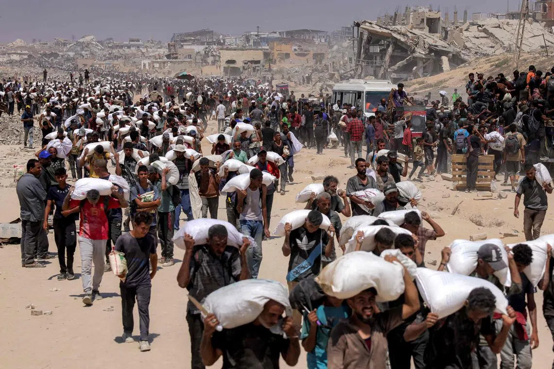 People carrying sacks of flour, after trucks carrying humanitarian aid entered northern Gaza, on July 27, 2025.