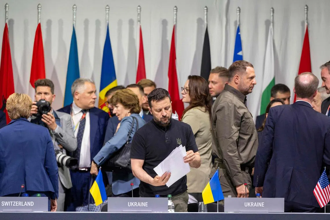 TOPSHOT - Ukraine's President Volodymyr Zelensky (C) looks at papers as he attends a plenary session at the Summit on peace in Ukraine, at the luxury Burgenstock resort, near Lucerne, on June 16, 2024. The two-day gathering brings together Ukrainian President and more than 50 other heads of state and government, to try to work out a way towards a peace process for Ukraine -- albeit without Russia. (Photo by URS FLUEELER / POOL / AFP)