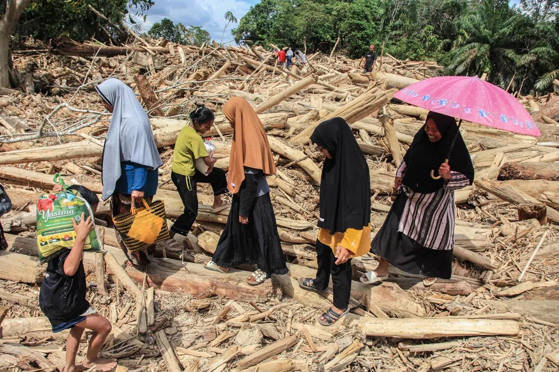 People carrying their belongings, walk among logs swept away by a flash flood in Aceh.