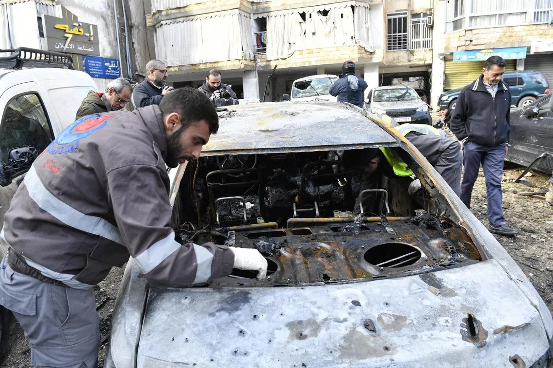 Civil Defence officials inspect a vehicle that was damaged near the building in Beirut, hit by a drone strike that killed Hamas deputy chief Saleh al-Arouri..