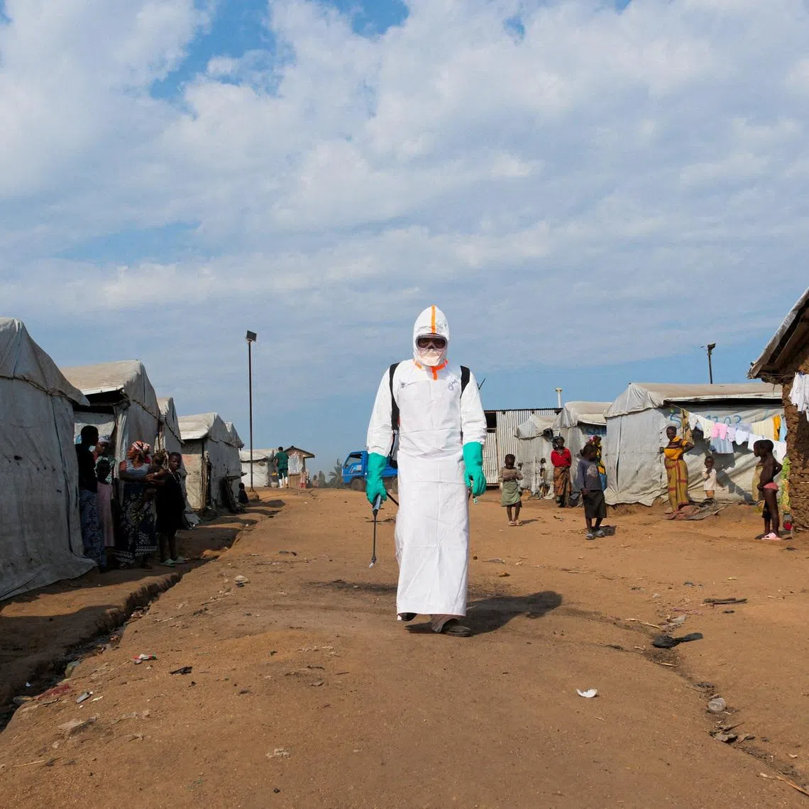 Displaced people watch a health worker in full personal protective equipment (PPE) preparing to disinfect the area during the burial of suspected Ebola victims at the Kigonze displaced persons camp in Bunia, eastern Democratic Republic of Congo, on June 18, 2026, one month after the outbreak was declared. REUTERS/Gradel Muyisa Mumbere