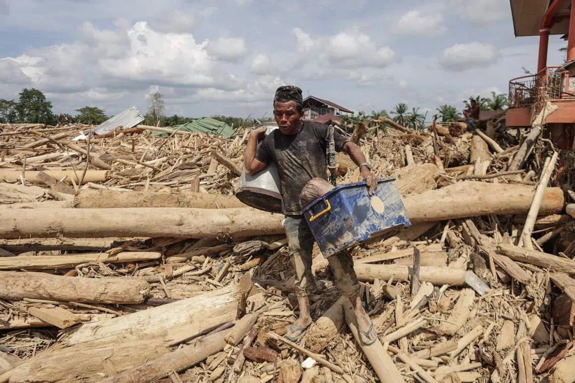 A man carries belongings he recovered from among piles of uprooted trees swept by the flash flood in Aceh Tamiang, Northern Sumatra, on Dec 11.