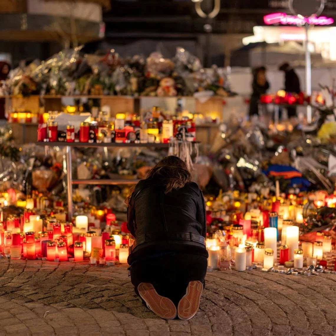 A woman lights a candle at a makeshift memorial outside the \"Le Constellation\" bar, after a deadly fire and explosion during a New Year's Eve party, in the upscale ski resort of Crans-Montana in southwestern Switzerland, January 5, 2026. REUTERS/Umit Bektas