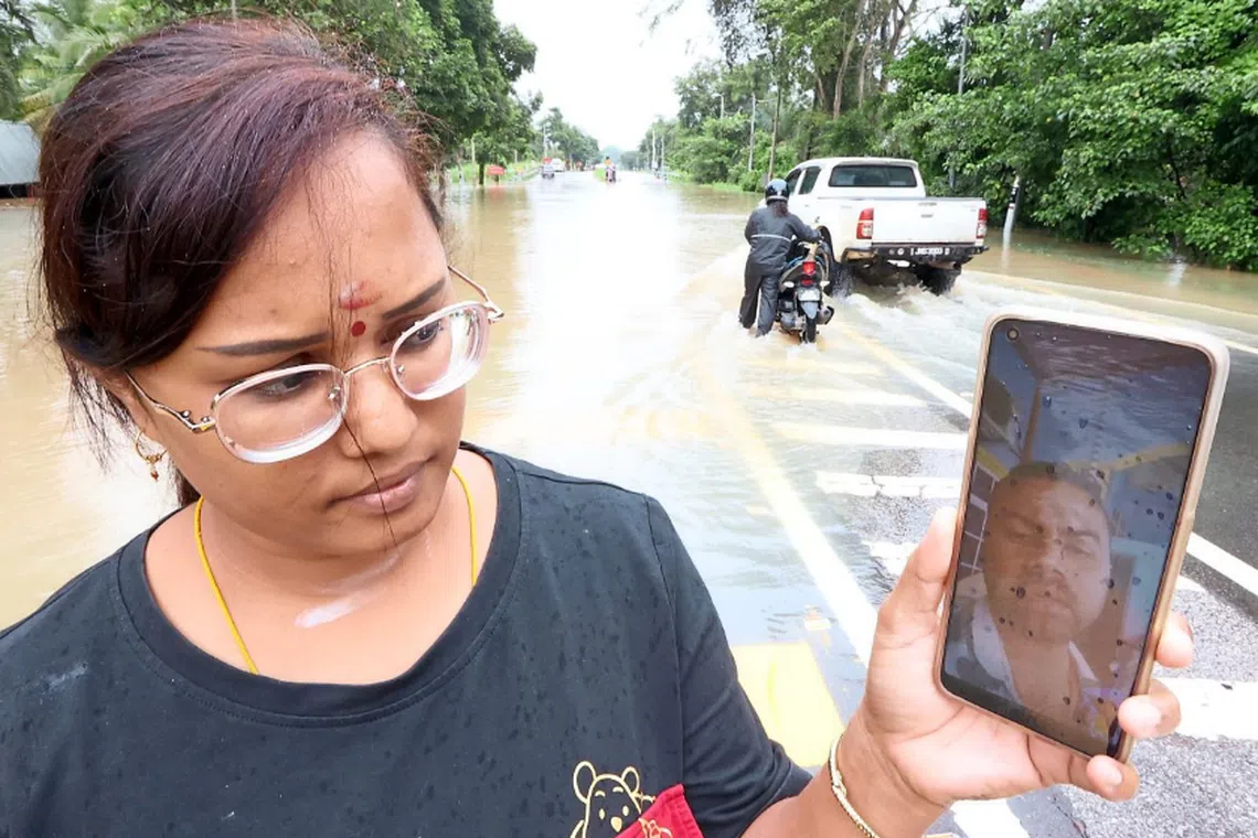 Ms Komathy talking to her brother N. Satha Sivam, 37, via a video call while the background is the submerged road connecting Yong Peng and Chaah