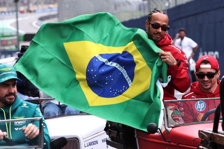 Ferrari's Lewis Hamilton holds a Brazil flag with Ferrari's Charles Leclerc and Aston Martin's Fernando Alonso during the drivers parade before the race.