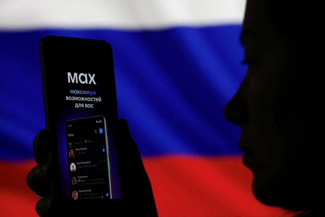 FILE PHOTO: A woman holds a smartphone displaying a web page of the Russian messenger application MAX next to a screen showing the state flag of Russia in this illustration taken September 4, 2025. REUTERS/Ramil Sitdikov/Illustration/File Photo