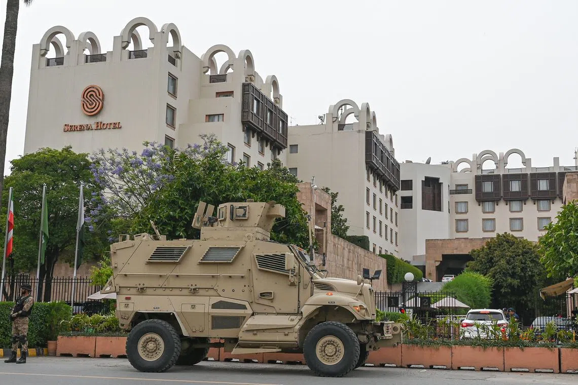 A security personnel (L) stands guard next to an armoured vehicle in front of a hotel in Islamabad on May 5, 2023, as security tightens in Pakistan's capital ahead of the foreign ministers meeting of Pakistan, China and Afghanistan. (Photo by Farooq NAEEM / AFP)
