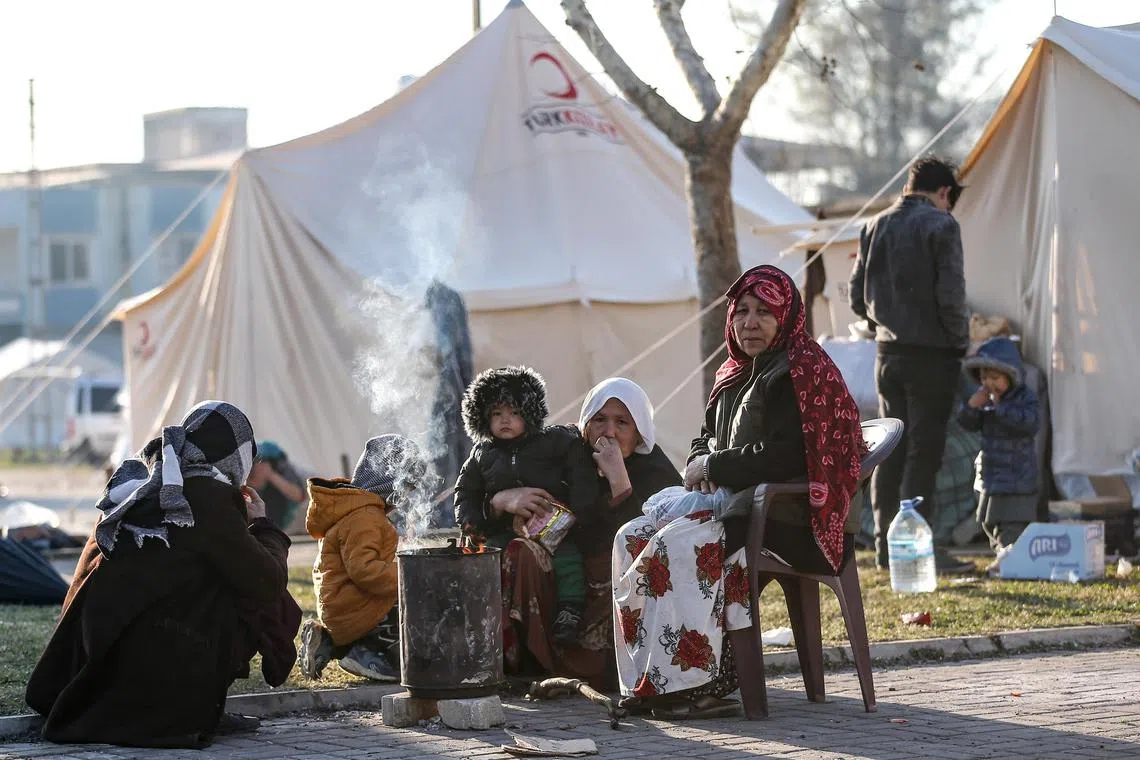 People sit outside a tent following a major earthquake in Hatay, Turkey. Tents are being erected in stadiums and shattered city centres, beach resorts outside the quake zone are opening up hotel rooms for evacuees.