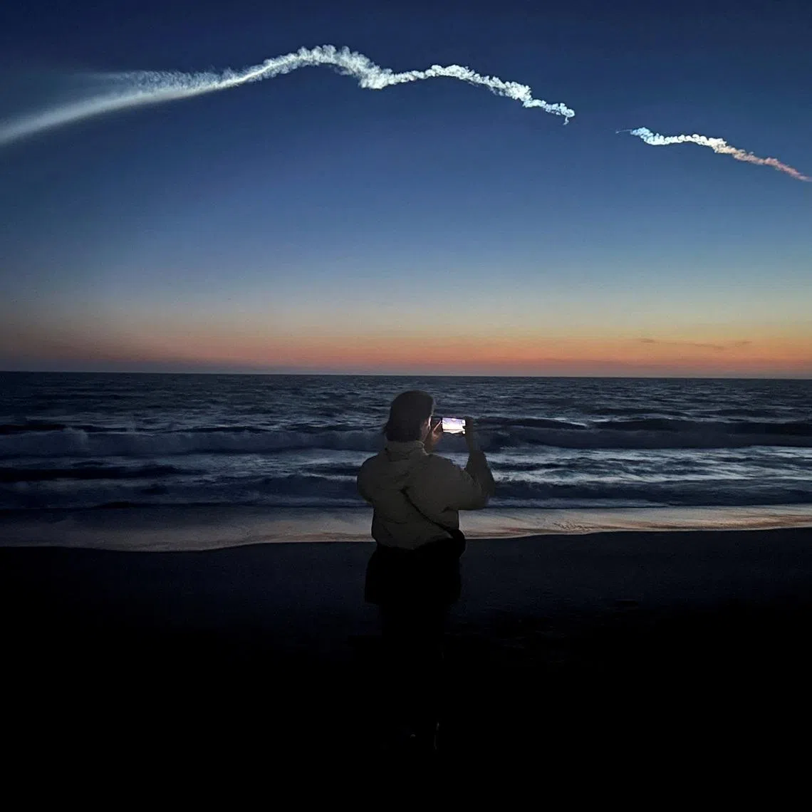 FILE PHOTO: A person takes photos of a trail as the Falcon 9 carrying Starlink satellites streaks across the sky in the latest SpaceX launch as viewed from Venice Beach in Los Angeles, California, U.S., April 6, 2026.   REUTERS/Daina Beth Solomon/File Photo