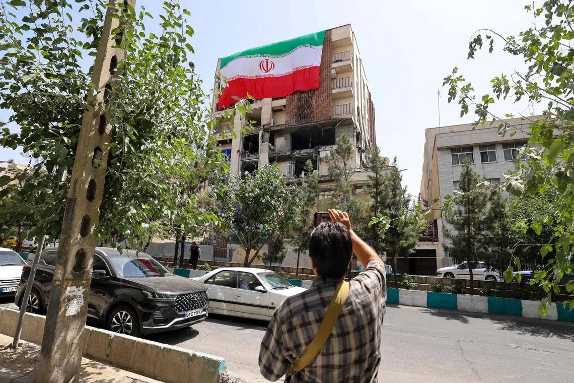 A man taking a photo of a residential building in Tehran that was hit by an Israeli missile, with the damaged part covered by a large Iranian flag, on June 25.