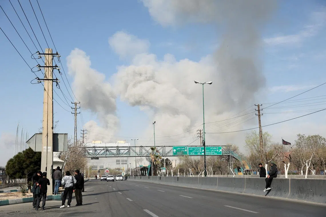 People gather on the sides of a road as smoke rises in the background following an explosion, amid the U.S.-Israeli conflict with Iran, in Tehran, Iran, March 5, 2026. Majid Asgaripour/WANA (West Asia News Agency) via REUTERS