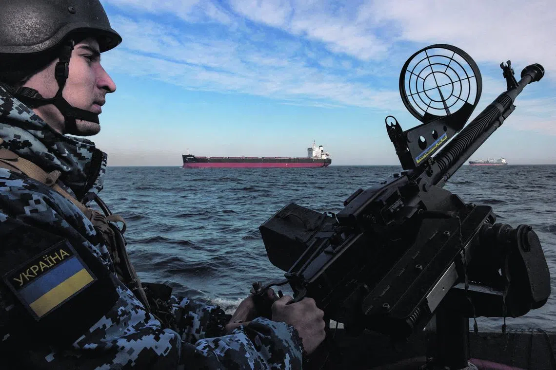 A serviceman of Ukraine's coast guard mans a gun on a patrol boat as a cargo ship passes by in the Black Sea on Feb 7, 2024.