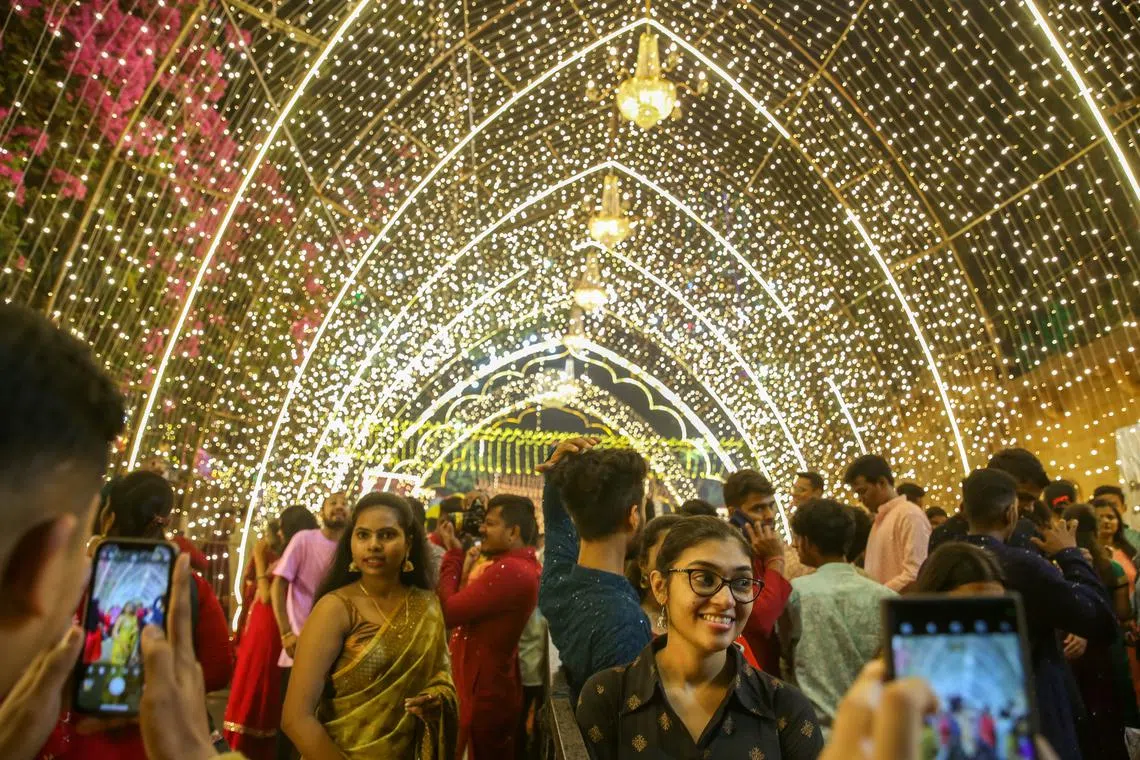 People posing for pictures under a light tunnel as streets are lit up with lanterns and lights on the occasion of the Diwali festival in Mumbai, India on Nov 12, 2023. 