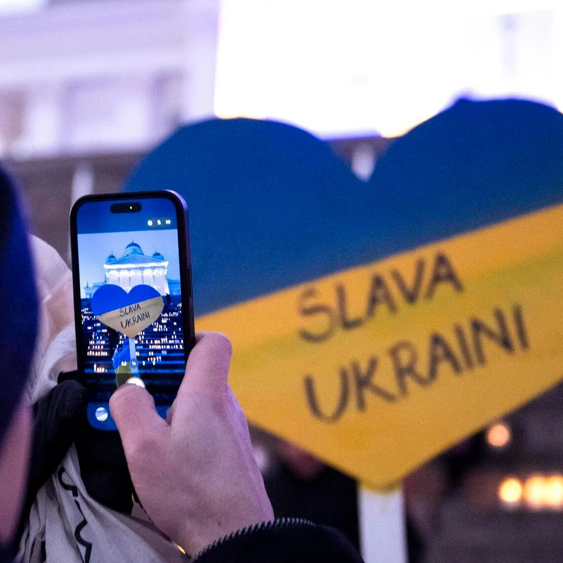 A person taking a picture of a sign featuring the colours of the Ukrainian flag and words that read "Glory to Ukraine", during a rally in support of Ukraine in Finland on Feb 24, the fourth anniversary of Russia's full-scale invasion of its neighbour.
