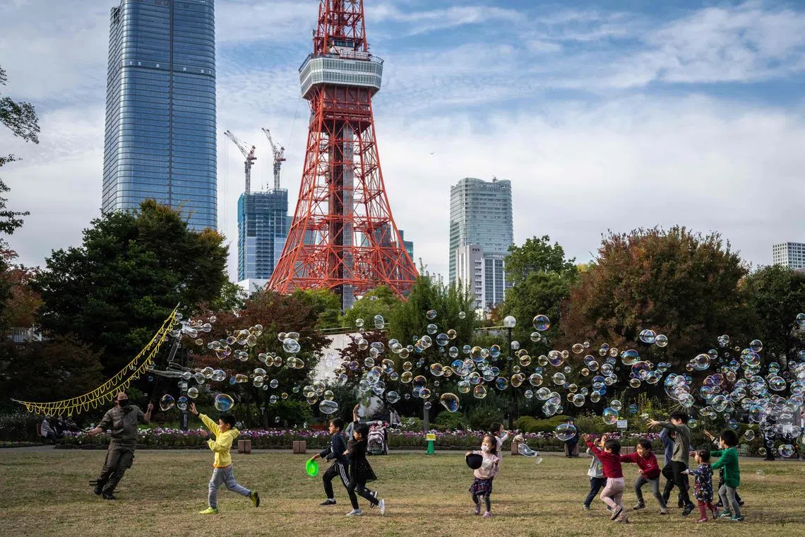 Children play with bubbles as the Tokyo tower looms in the background in Tokyo on November 10, 2022. (Photo by Yuichi YAMAZAKI / AFP)