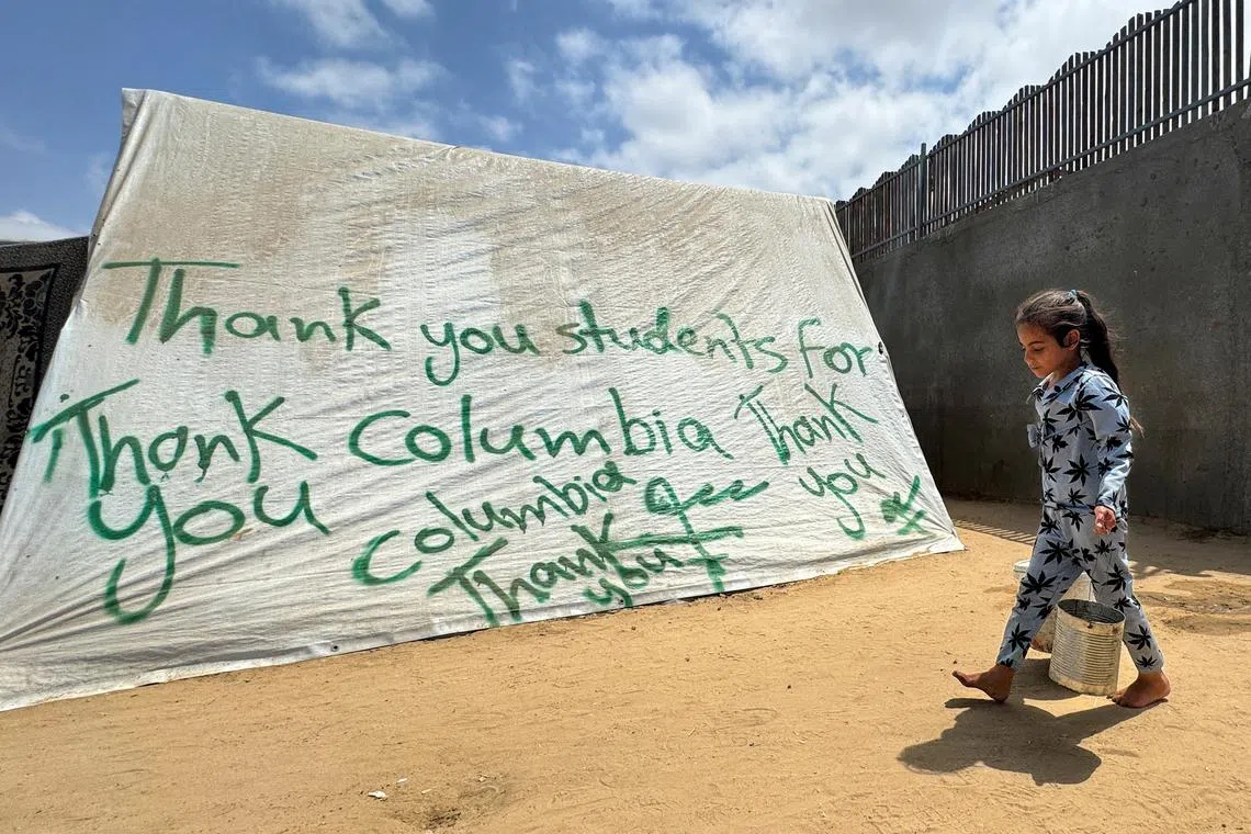 FILE PHOTO: A girl walks next to a tent sprayed with a message in solidarity with pro-Palestinian university students, amid the ongoing conflict between Israel and Palestinians, in Rafah in the southern Gaza Strip, May 2, 2024. REUTERS/Mohammed Salem/File Photo