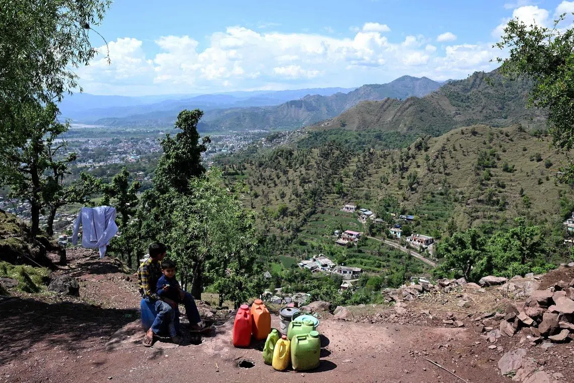 Children sitting next to water-containers atop a hill, at the frontier district of Poonch in India's Jammu region.