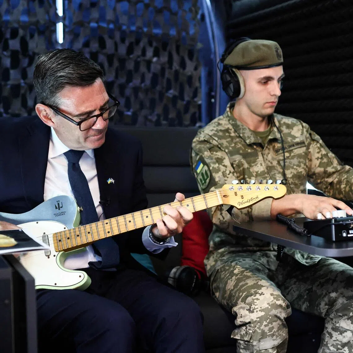 Britain’s Prime Minister Andy Burnham (left) plays the guitar next to a Ukrainian soldier in the back of a soundproofed van.