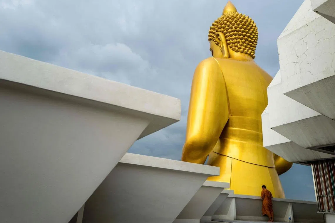 A Thai Buddhist monk looking at the Phra Dhammakaya Thep Mongkol, a giant seated Buddha statue, as he visits a pagoda at the Wat Paknam Phasi Charoen temple in Bangkok, Thailand on May 19, 2026. 