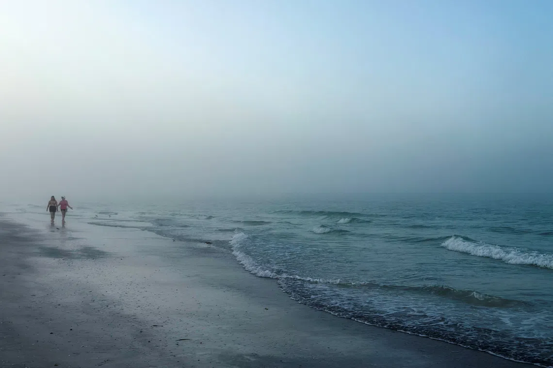 People walking along the beach at the barrier island of Lido Key, during the early morning fog in Sarasota, Florida, US, on Nov 9, 2025.