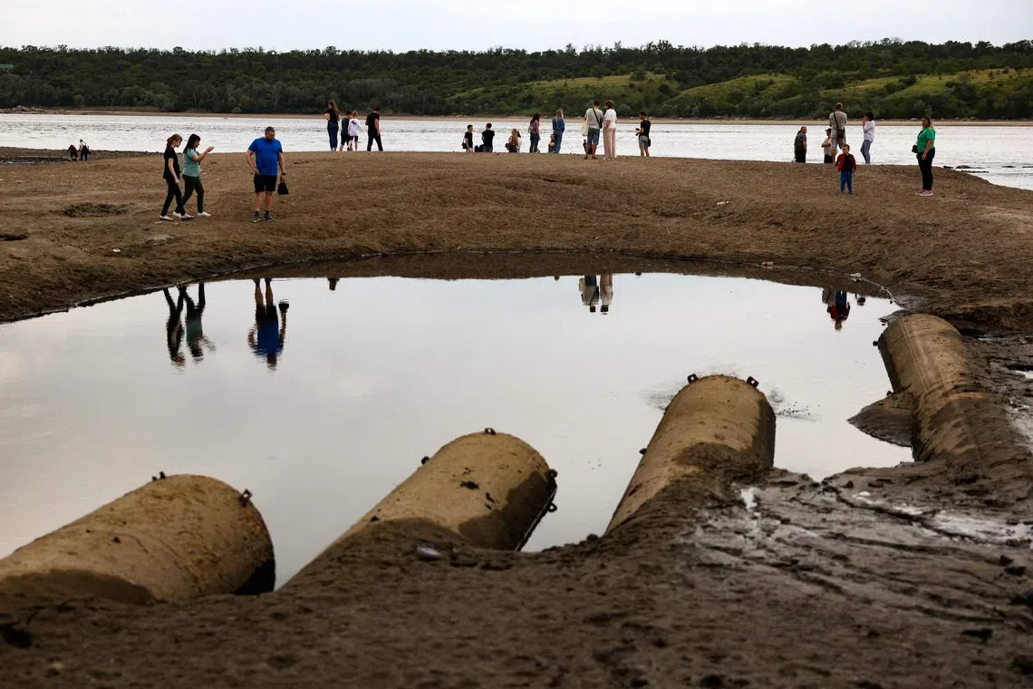Residents of Zaporizhzhia walk through the mud of the Dnipro river on Saturday following damage sustained at the Nova Kakhovka hydroelectric power plant dam earlier in the week. 