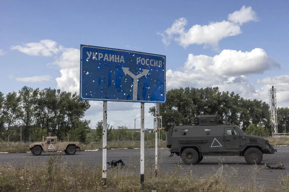 Ukrainian military vehicles pass a sign reading Ukraine, left, and Russia near the destroyed Russian border post on the Russian side of the Sudzha border crossing with Ukraine.