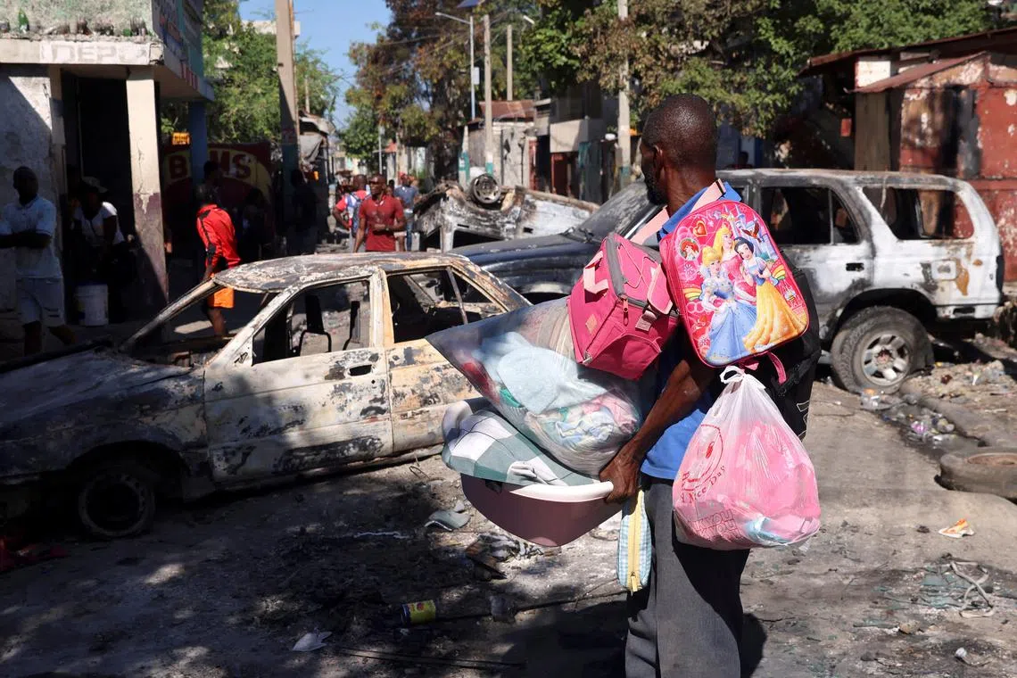 FILE PHOTO: A man carrying his belongings observes the wreckages of vehicles burnt over the weekend by armed gangs in Port-au-Prince, Haiti December 9, 2024. REUTERS/Ralph Tedy Erol/File Photo