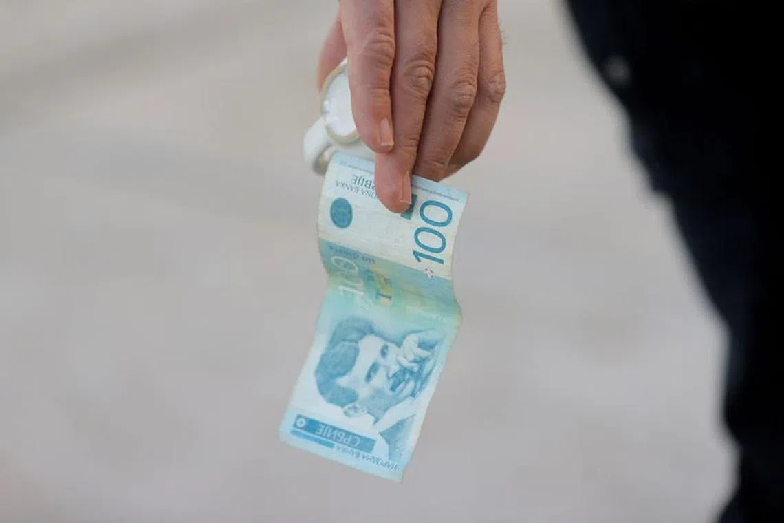 A man holds a dinar currency and a coffee cup in Mitrovica, Kosovo, February 1, 2024.  REUTERS/Valdrin Xhemajj/file photo