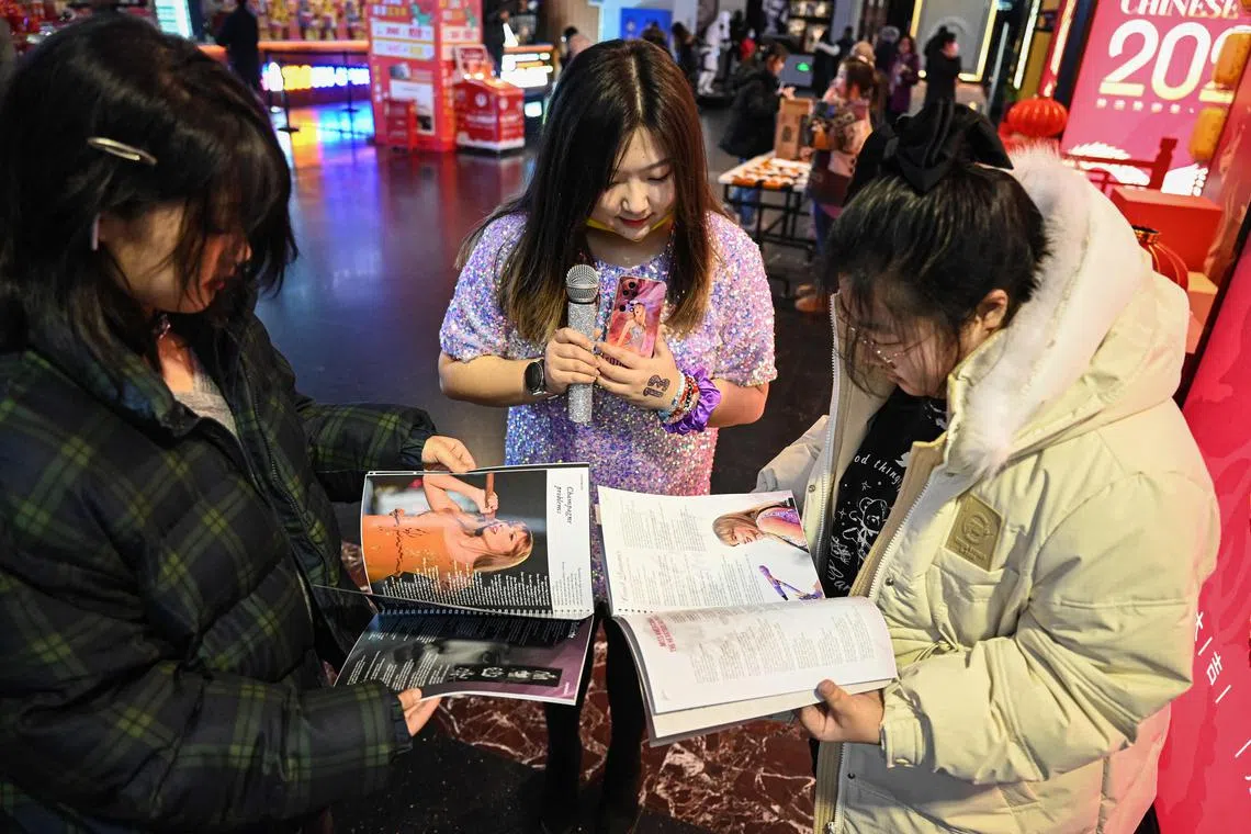 This photo taken on February 3, 2024 shows Chinese fans reading a lyrics book of US singer Taylor Swift before watching concert film "Taylor Swift: The Eras Tour" at a cinema in Beijing. Waving glow sticks, and sporting sequin dresses and friendship bracelets, Chinese fans of American pop sensation Taylor Swift turn a normally-quiet Beijing cinema into a raucous celebration of their favourite singer. (Photo by Jade GAO / AFP) / To go with AFP story "China-entertainment-music-Swift-fans", SCENE by Luna LIN (STF)