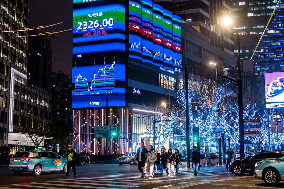 People cross a street in front of a large screen displaying the latest stock exchange and economy data, in Shanghai, China, 11 March 2025. Asian stock markets plunged amid concerns over a potential recession in the US triggered by President Trump's tariffs.  EPA-EFE/ALEX PLAVEVSKI