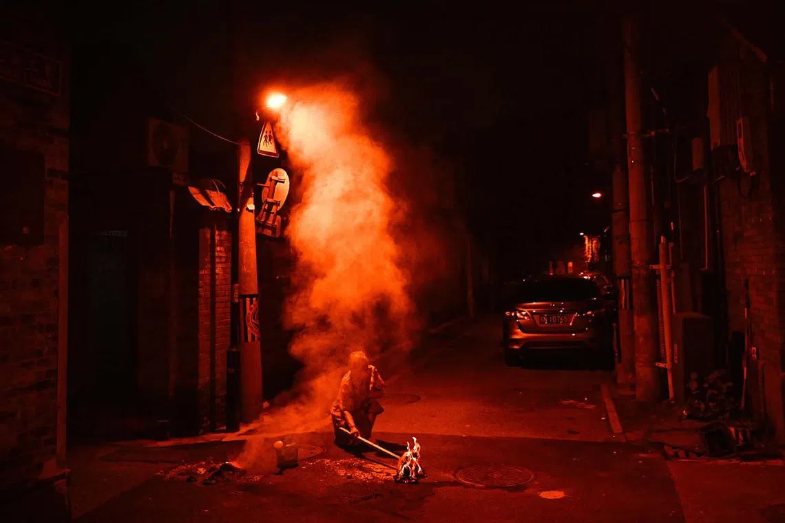 TOPSHOT - A woman burns offerings for her dead ancestors on a street during the Hungry Ghost Festival in Beijing on August 18, 2024. The festival is celebrated in the seventh lunar month of the lunar new year calendar among communities in southern China, Malaysia, Singapore, Hong Kong and Taiwan, marks the belief that the "Gates of Hell" are opened to let out the hungry ghosts who then wander in the land of the living while foraging for food. During the festival food offerings are made while paper money and joss sticks are burnt outside homes to keep the spirits of dead ancestors happy and to bring good luck. (Photo by Pedro Pardo / AFP)