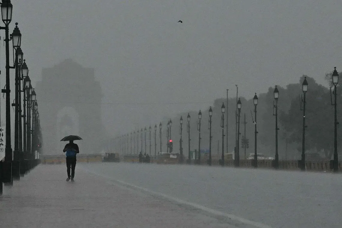 A man holding an umbrella walks at the India Gate during heavy rainfall in New Delhi on June 29, 2024. (Photo by Arun SANKAR / AFP)